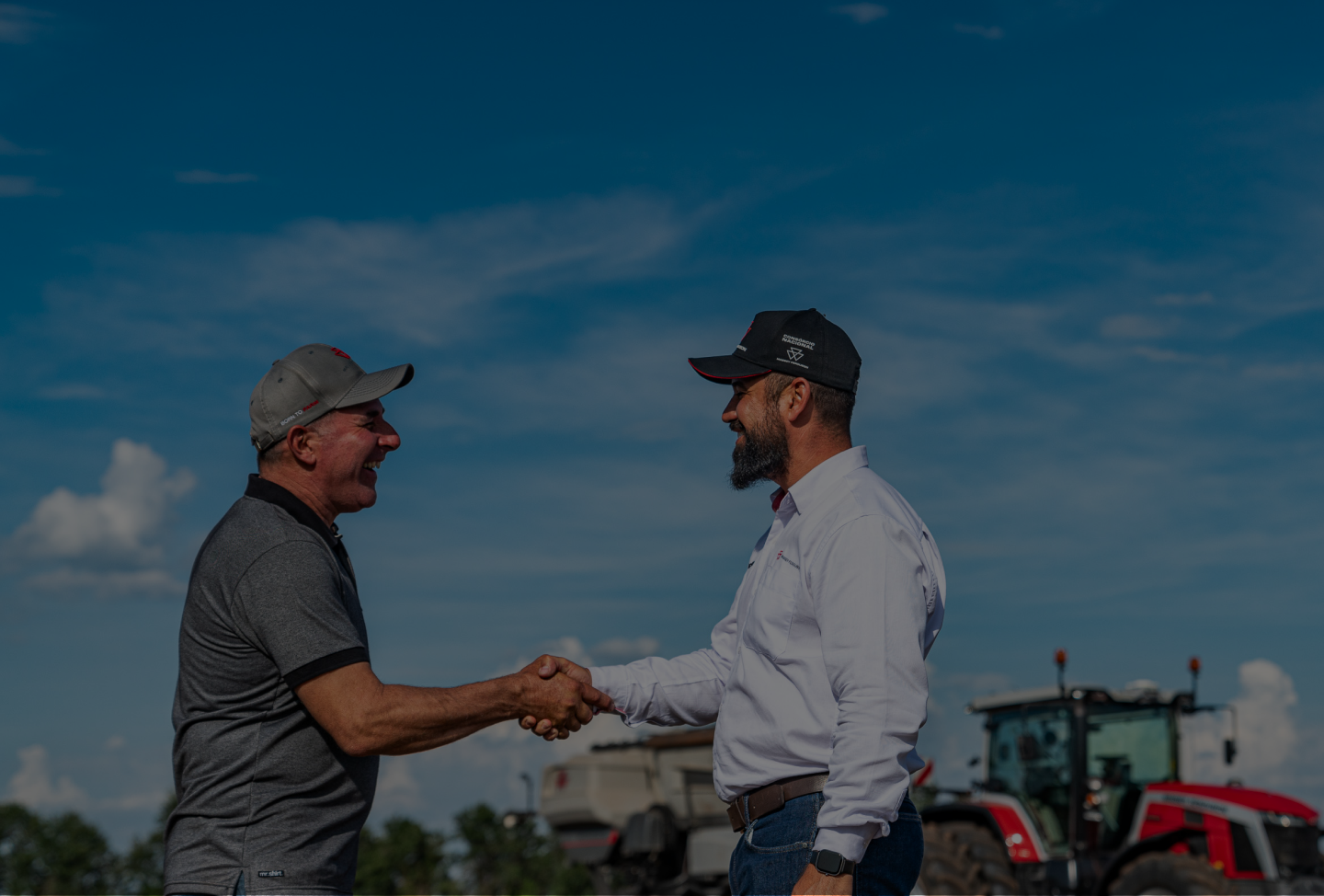 A dealer and customer shaking hands in a field in front of a Massey Ferguson tractor.